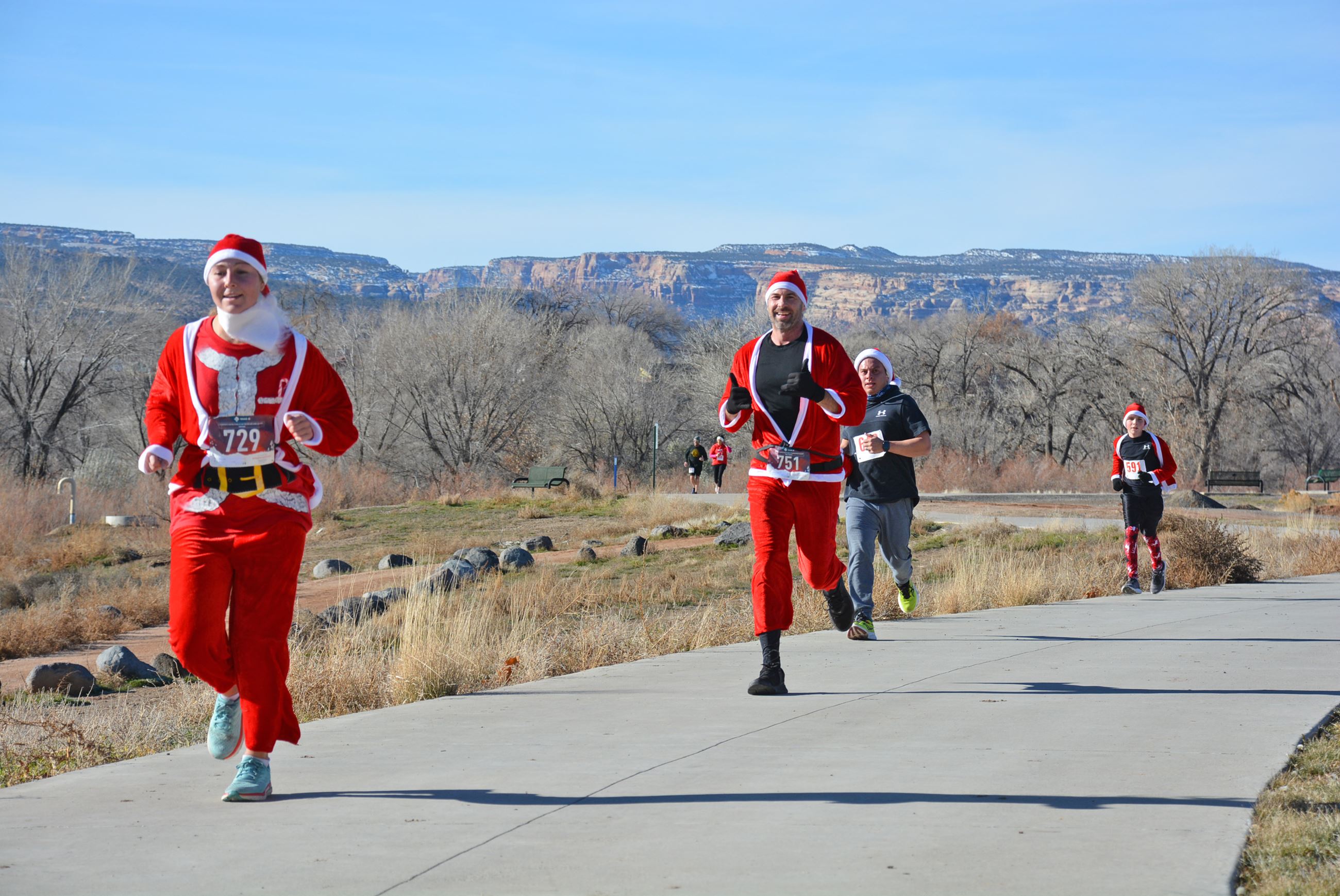 Four people dressed in Santa suits running on a path